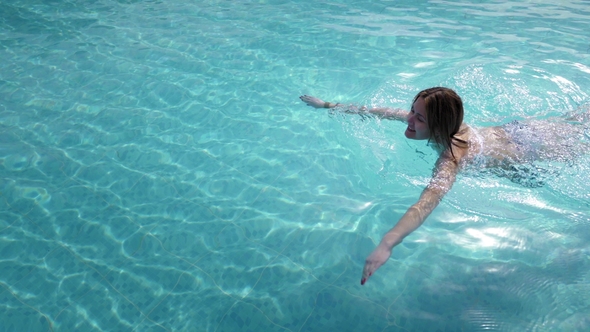 Beautiful Caucasian Model, Young Woman Is Swimming in a Pool with Blue Water in a Hotel