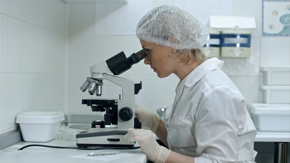 Cute Female Medical Researcher Writing Notes While Using Her Microscope in a Laboratory alt