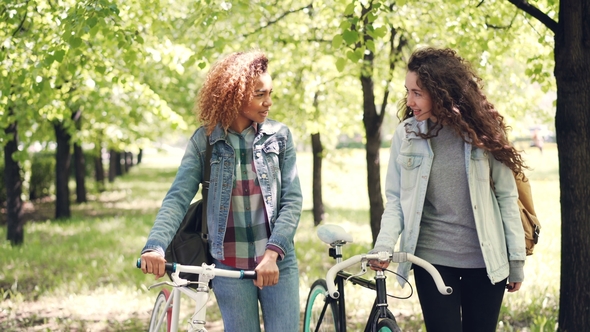 Dolly Shot of Cheerful Girls Friends Walking in Park with Bikes Relaxing After Riding Bicycles and
