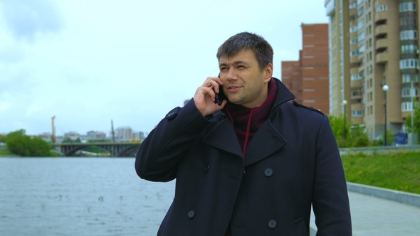 A Man Is Talking on a Mobile Phone Against the Backdrop of a Cityscape.