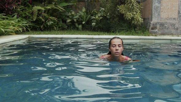 Sexy Slender European-looking Girl with a Chocolate Tan in a Pink Swimsuit Swims in the Pool