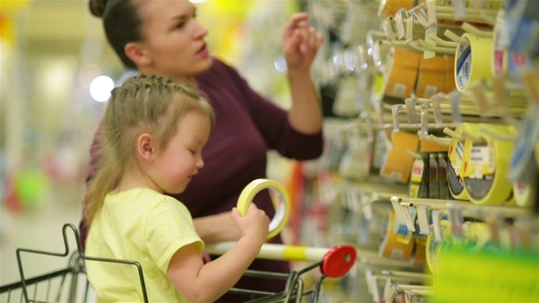 Smiling Mother and Daughter at the Supermarket. A Daughter Helps Her Mother Choose an Adhesive Tape