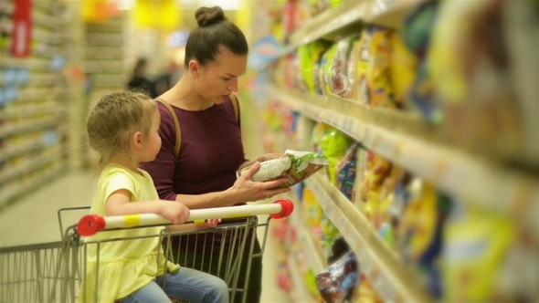 Mother and Daughter Shopping in Supermarket. They Are Buying a Breakfast Flakes. A Daughter Sitting