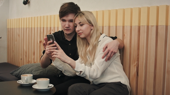 Happy Couple in a Coffee House Having Breakfast and and Using Cell Phone