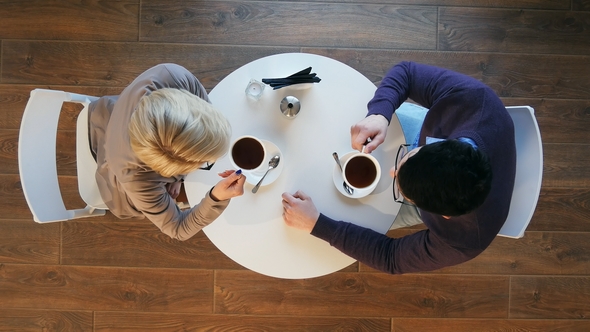 Happy Young Couple Drinking Coffee and Talking in Coffee Shop