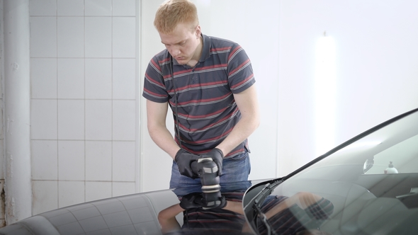 Redhead Male Worker Is Processing Surface of Car By Polishing Machine in a Car-service, Covering By