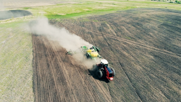 Agricultural Tractor Is Sowing Ground in a Cloud of Dust.