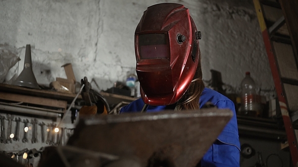 Cute Welder Girl in Uniform in the Garage Working with Welding Equipment. Women's Work in Art