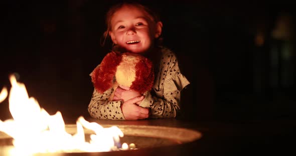 A young girl enjoys a fire with her stuffed animal puppy.