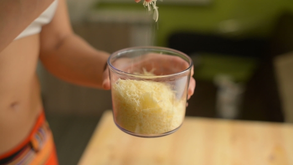 A Young Girl Rubs Cheese in a Special Mechanical Grater with a Transparent Glass on a Wooden Table