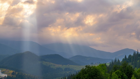 Sun Rays Pass through the Clouds Over the Mountains at Sunset