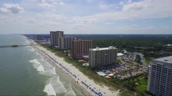 Drone flying away from beach and ocean front resorts over the ocean on sunny day