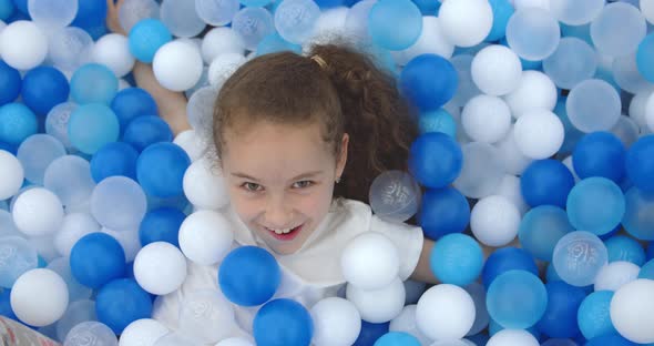 Portrait of a Cheerful Little Girl Smiling Child Jumps Out of Children's Plastic Ballskid Looks at