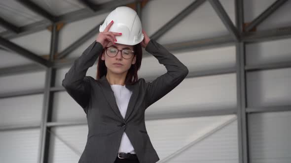 A Young Woman Puts on a Protective Helmet and Shows a Thumb at a Construction Site. The Boss in a