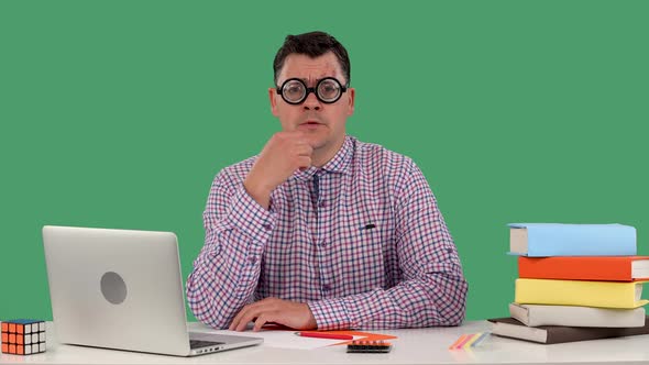 A Man Sits at a Desk in Front of a Laptop and Books Thinks About Something Nods His Head Negatively