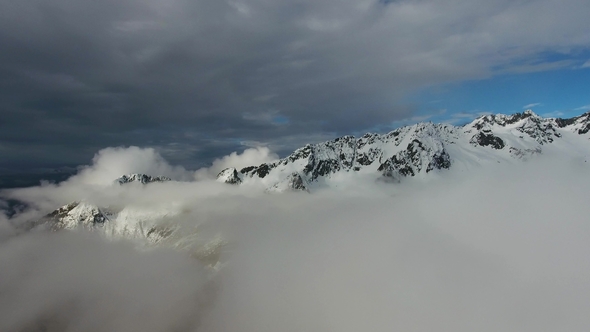 Flying in Clouds Between Snow-capped Mountains