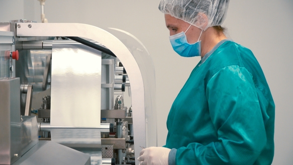 Worker in Mask and Protective Uniform Control the Process of Sorting Capsules
