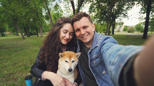 Young Wife and Husband Are Taking Selfie with Adorable Dog Kissing and Hugging Each Other