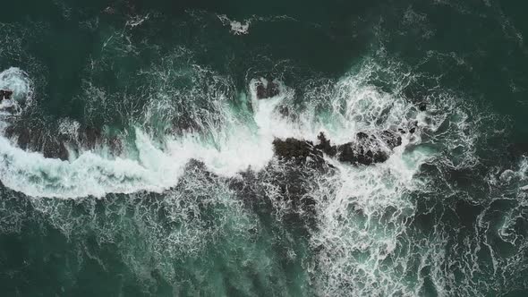 Aerial top down view of waves splashing into rocks in the sea, super slow mot