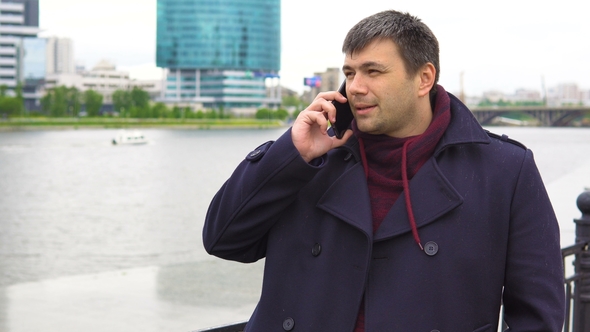 A Man Is Talking on a Mobile Phone Against the Backdrop of a Cityscape.
