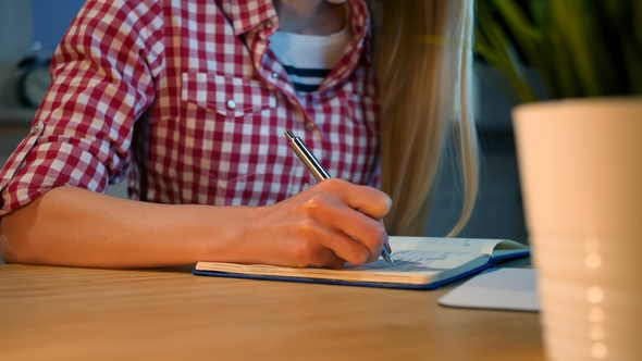 Female Writing with Pen in Notepad. Crop View of Woman with Long Blond Hair in Bright Casual Shirt