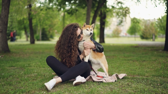 Happy Girl Proud Dog Owner Is Caressing and Kissing Her Pet Sitting on Grass in the Park