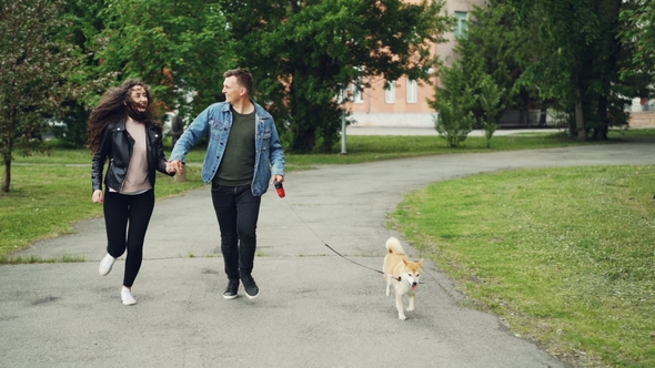 Dolly Shot of Cheerful Sporty People Dog Owners Running in the Park with Their Pet and Smiling