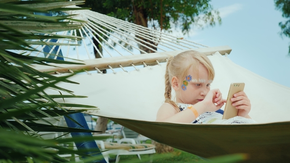 A Cool Girl with Aqua-grime Plays on the Phone in a Hammock in a Tourist Hotel