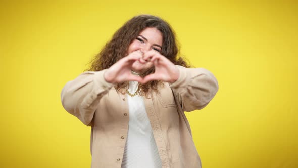 Portrait of Happy Caucasian Plussize Woman Showing Heart Gesture with Hands Looking at Camera