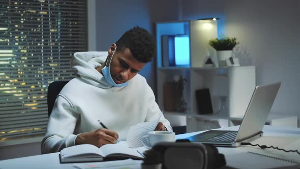 Mixedrace Man with Medical Mask Signing Documents in Home Office