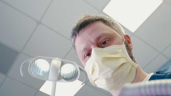 Doctor in a Mask Is Approaching To Patient and Beginning Surgery in Dentistry