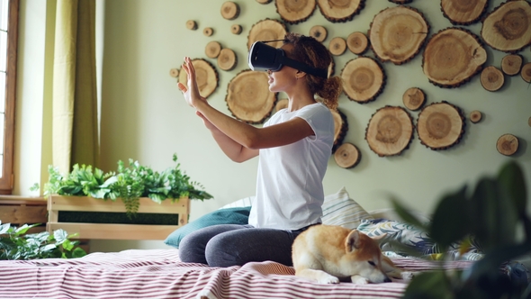 Smiling Mixed Race Girl Is Using Augmented Reality Glasses Moving Hands Sitting on Bed in Modern