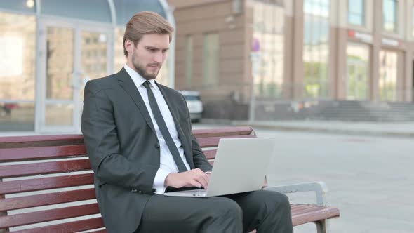 Young Businessman Pointing at the Camera While Sitting on Bench Outdoor