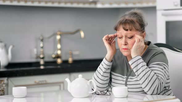 Middle Aged Woman Massaging Temple Having Headache in Kitchen at Home