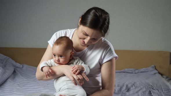 Brunette Mother Caresses Cute Newborn Boy Sitting on Bed