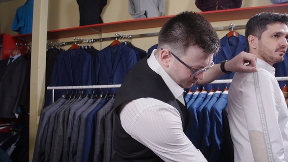 Man Helps Another Try on a Suit in a Clothing Store