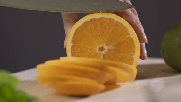 Woman Cutting Orange with a Knife on a Kitchen Table. Woman Making Orange Fresh Juice.