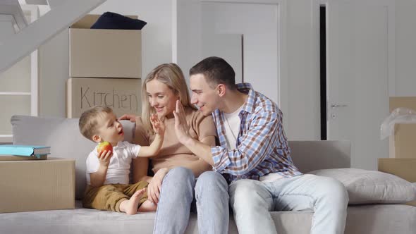 Happy Family Householders with Kid Sitting on Couch at New Home at Moving Day