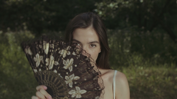 Portrait of Enigmatic Woman with Hand Fan Outdoors