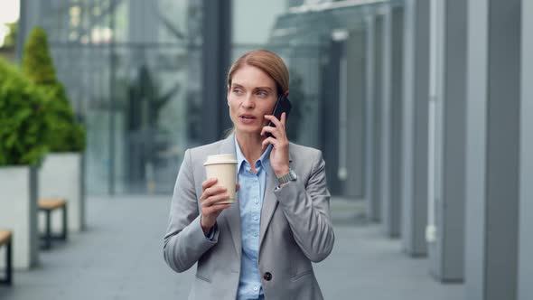 Business Woman Talking with Partners on Mobile Phone and Drinking Coffee Walking Near Office