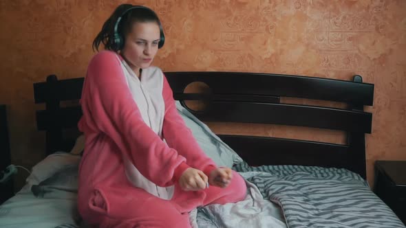 Girl in Pajamas on the Bed Listens to Music Through Headphones and Dances Slowmo