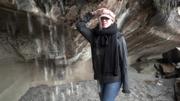 Female traveler walking under waterfall cliff