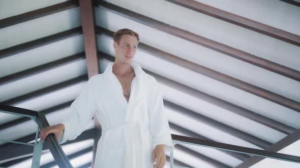 Handsome Man in White Bathrobe Goes Down Stairs in House