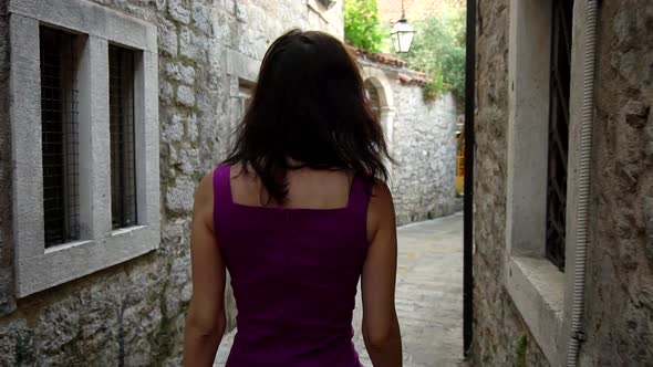 A Beautiful Brunette Girl Walks Along the Narrow Streets of the Old City and Looks at the Camera