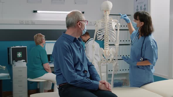 Nurse with Face Mask Explaining Bones on Human Skeleton