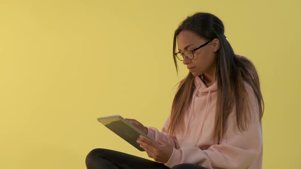 Black Woman in Eyeglasses Working on Tablet on Yellow Background