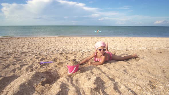 Little Baby Girl In A Bathing Suit And Sunglasses On Playing Sandy Beach