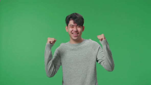 A Happy Asian Man Celebrating While Standing In Front Of Green Screen Background
