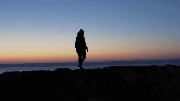 A silhoutte of a girl walking on rocks during blue hour. Slow motion.