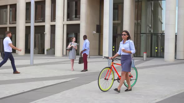 African Businesswoman Walking with Bicycle Near Modern Office Building Drinking Coffee